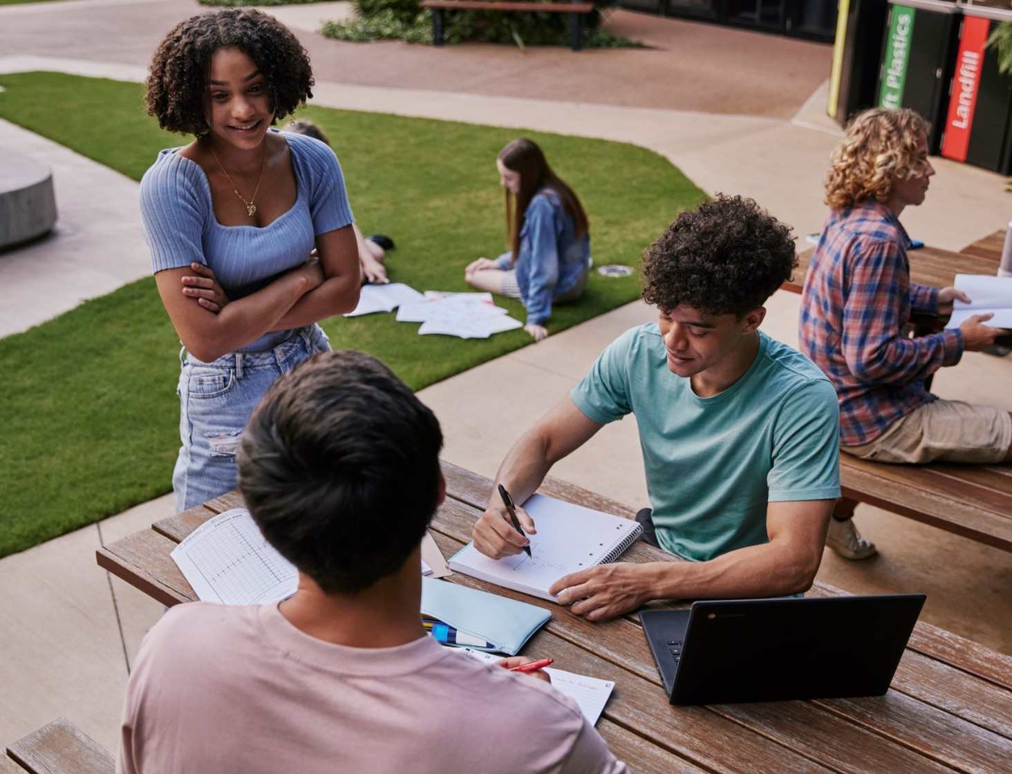 Some students discussing their homework while sitting on a school bench aside an HP laptop.