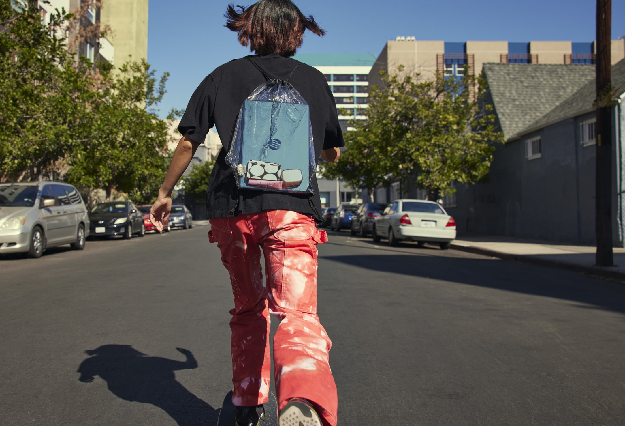 Ein Junge auf seinem Skateboard auf dem Weg zur Schule mit einem HP Laptop in seinem durchsichtigen Rucksack.