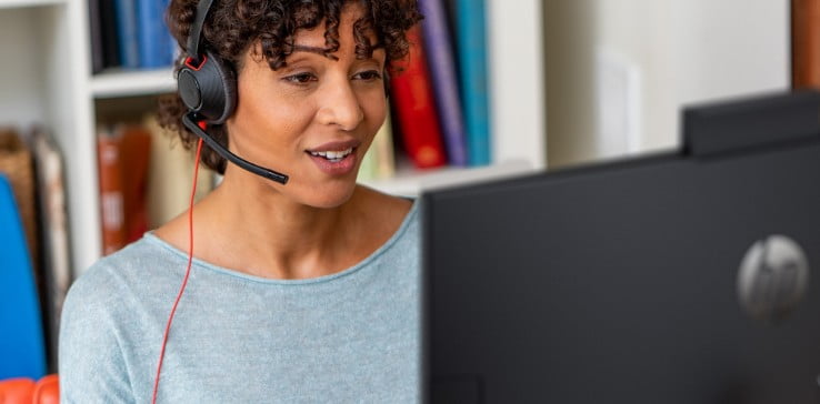 Woman wearing Poly Blackwire wired headset, seated at home office desk and engaged in a video call Woman wearing Poly Blackwire wired headset, seated at home office desk and engaged in a video call